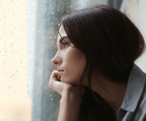 Woman with brown hair looking out the window which has rain drops on it