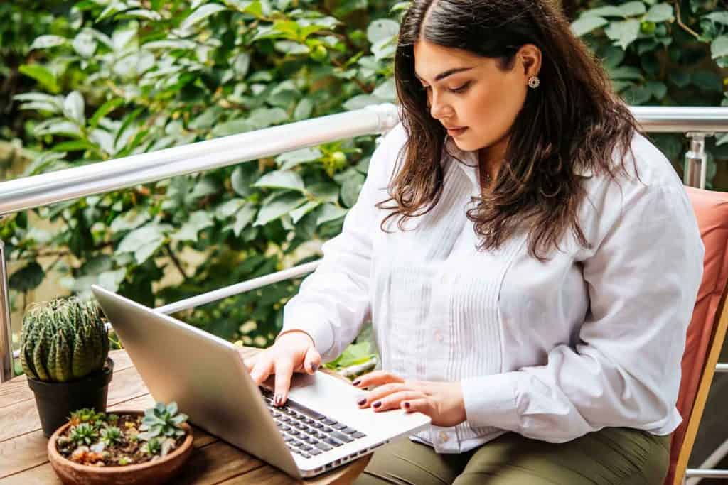 A Woman Searching For Plus Size Styling And Image Consulting Services Using A Small Laptop At A Table Outside