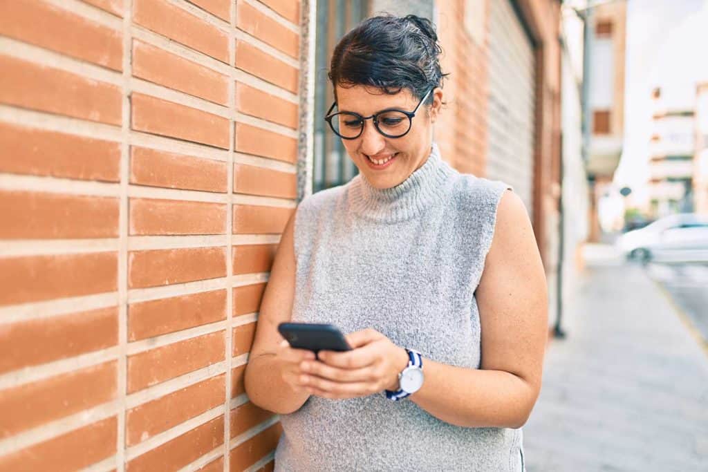 A Plus Size Woman Styled In A Sleeveless Turtleneck Looking At Her Phone And Smiling